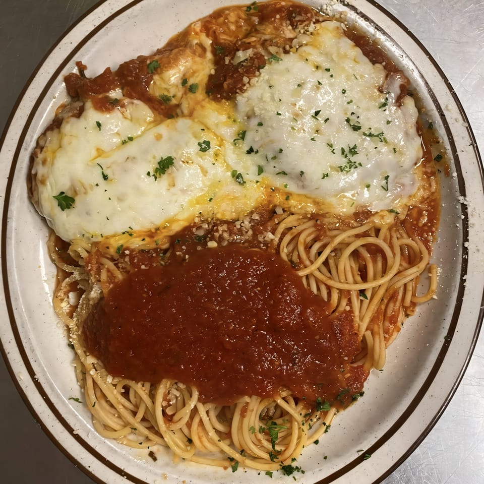 Chicken Parmesan with spaghetti and marinara sauce, topped with melted mozzarella and parsley.