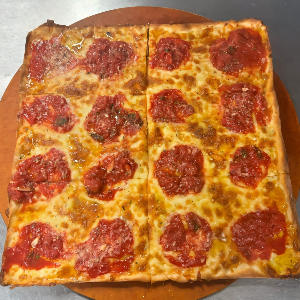 A square Bella Pizza pie, cut into four sections, with melted cheese and dollops of red sauce.