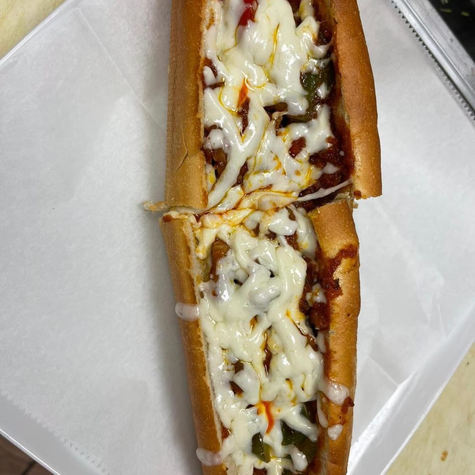 A Bella Pizza cheesesteak sub, cut in half, with melted cheese and meat filling.