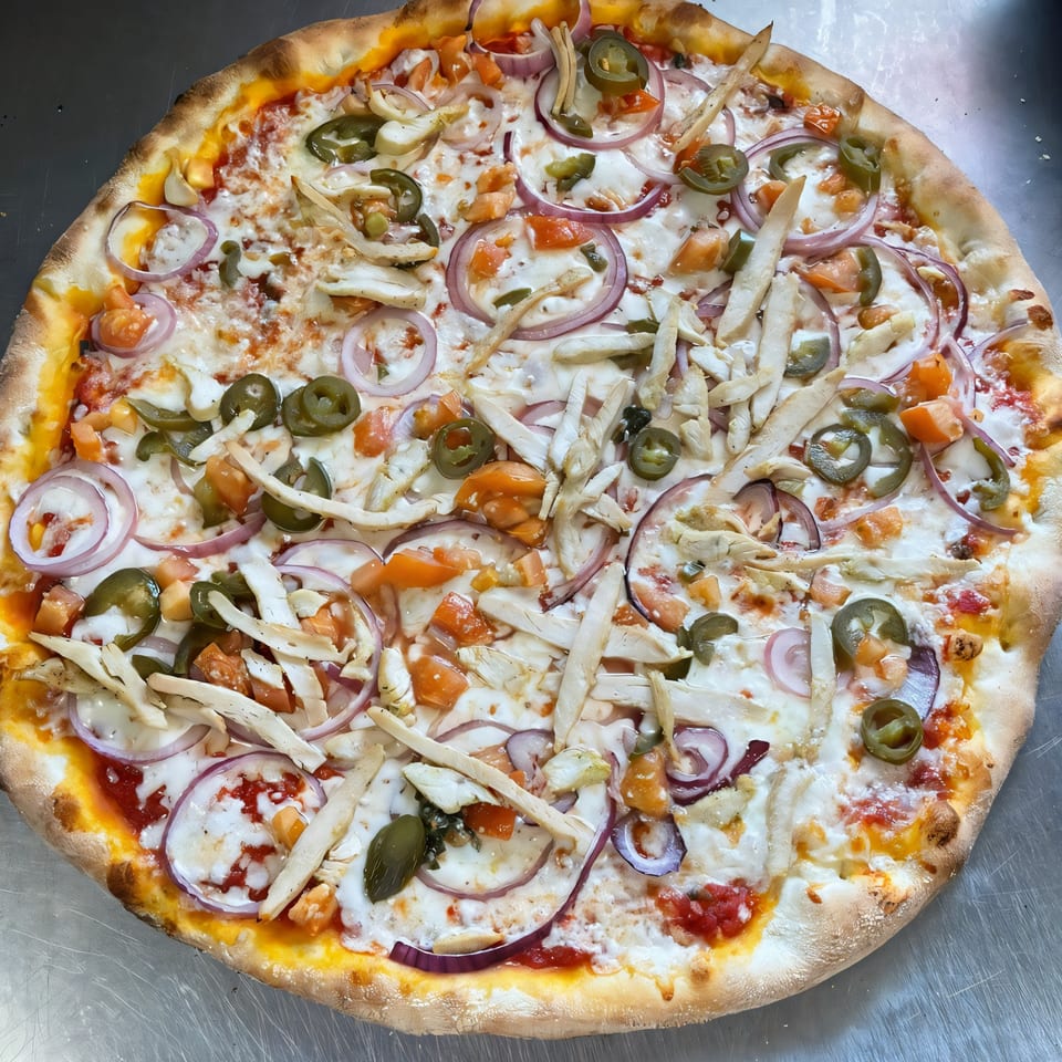 Bella Pizza's chicken pizza with red onions, jalapeños, and tomatoes on a metal surface.