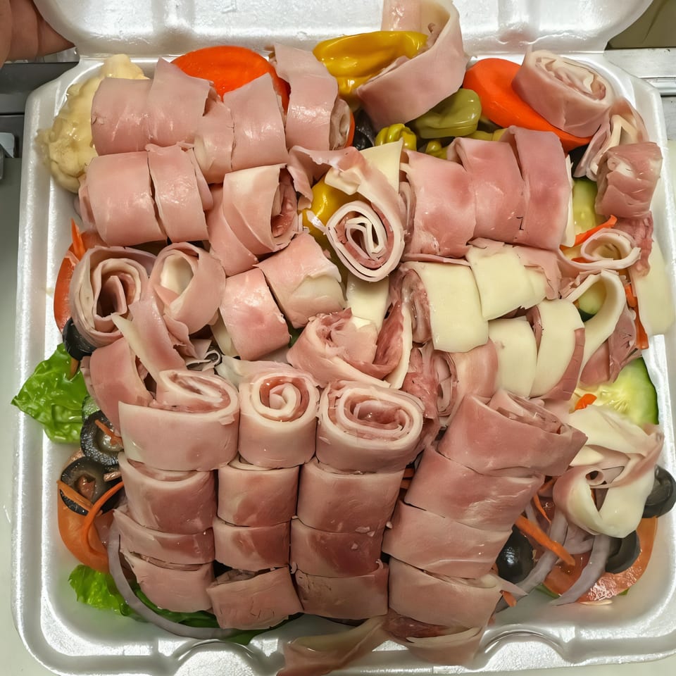 A large antipasto salad with rolled ham and cheese, olives, peppers, and lettuce in a styrofoam container.