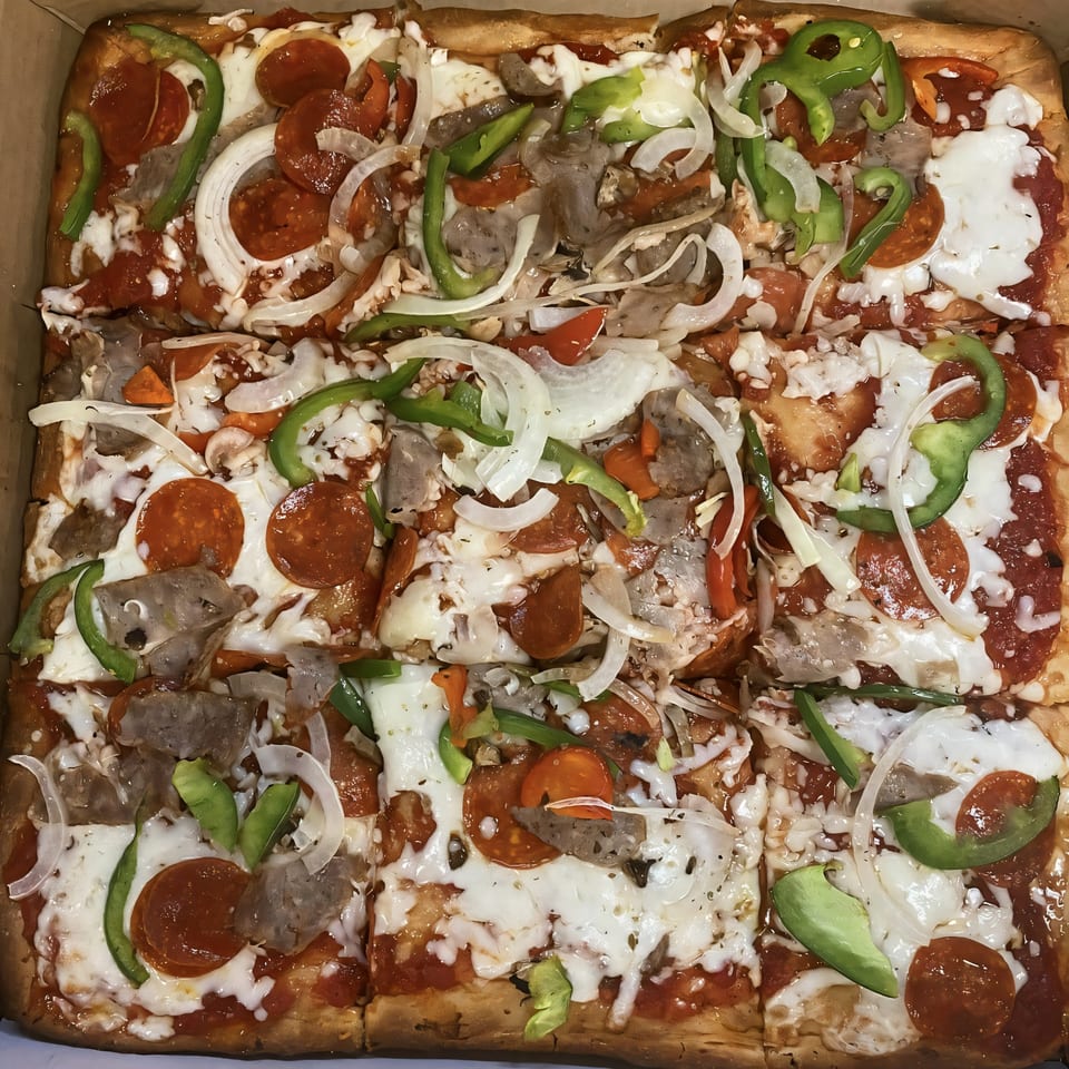A rectangular Bella Pizza with pepperoni, sausage, green peppers, and onions, cut into squares.