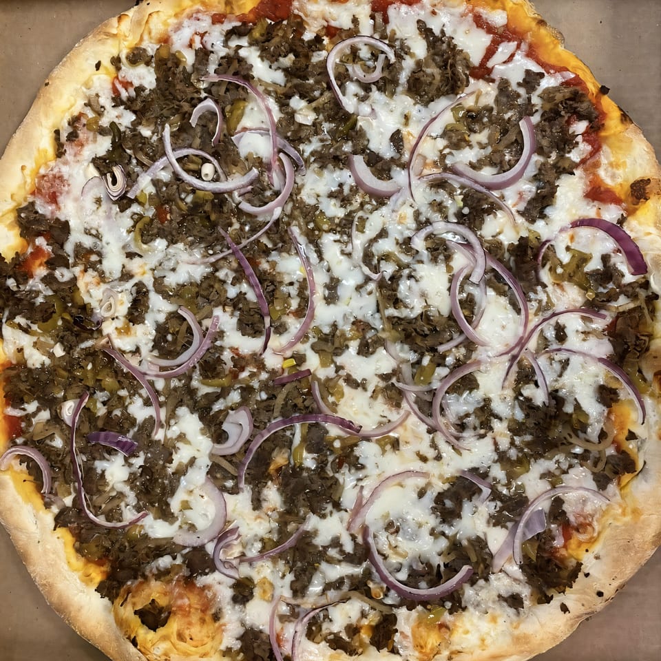 A Bella Pizza cheesesteak pizza, topped with steak, cheese, and red onion slices.